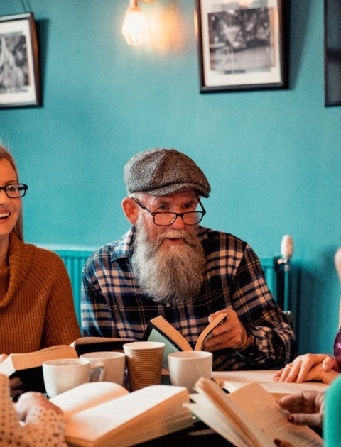 Five happy people sit around a table with hot drinks and books