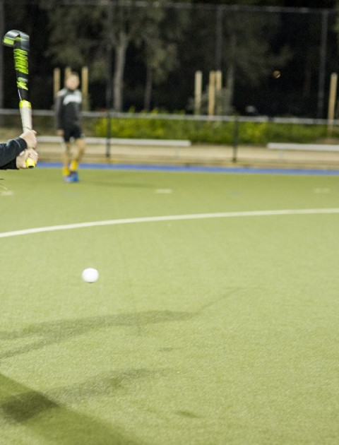 a girl wearing black sports kit is hitting a ball with a hockey stick