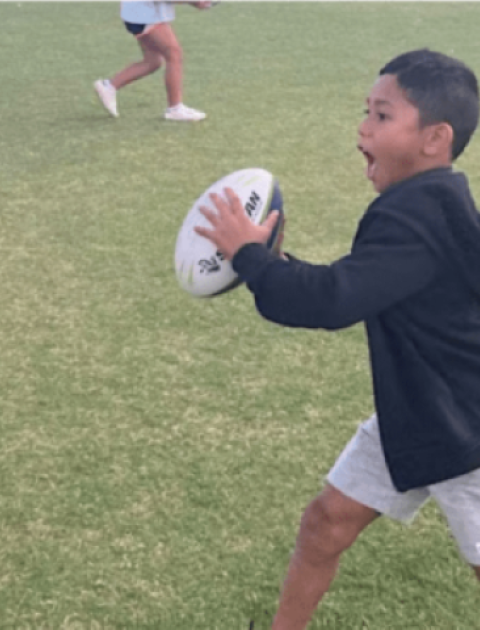 a boy holding a rugby ball is running at a tackle mat