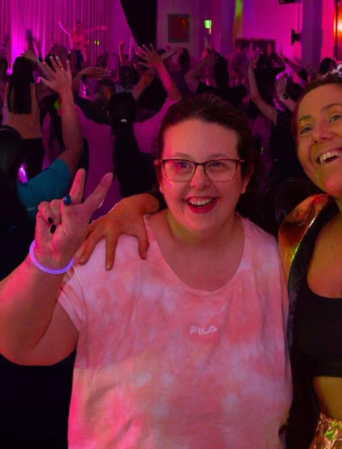 two women with their arms around each other are smiling at the camera in a darkened room