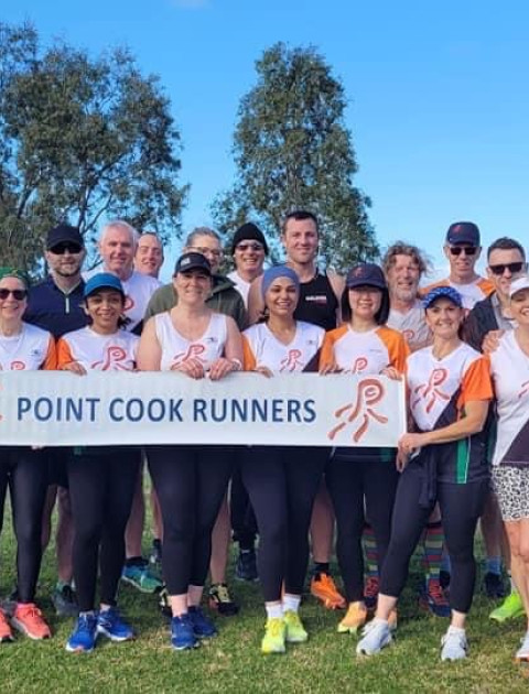 a group of people stand and smile at the camera holding a banner which says Point Cook Runners