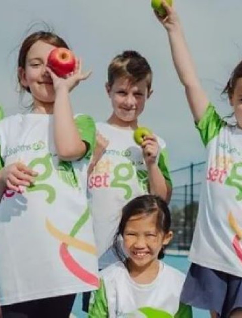 a group of kids in white and green NetSetGo T shirts are cheering at the camera
