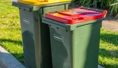A red lidded general waste bin placed next to a yellow lidded recycling bin on a kerbside. 