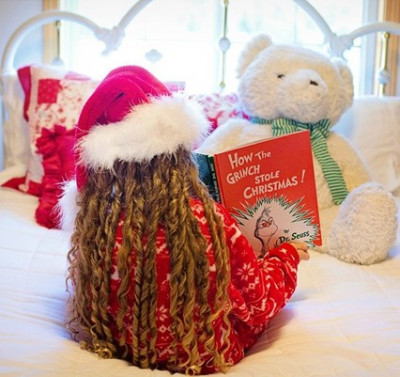 a child wearing a santa hat is reading how the grinch stole christmas to a teddy bear