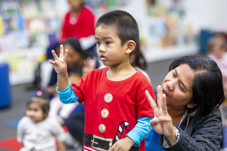 Boy watching presenter counting showing three fingers with mum