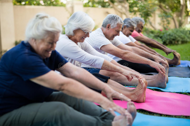 a line of people are sitting with their legs stretched out reaching for their toes