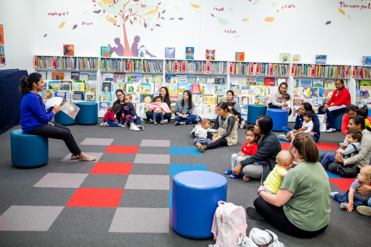 Toddlers and parents sitting down listening to a story in the library.