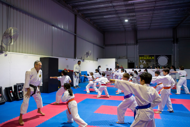 a karate class of children are all standing side on in a punch stance looking at their instructor