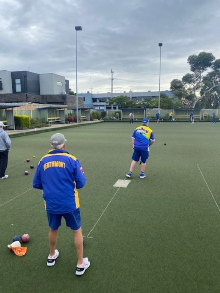 people are bowling down a green away from the camera