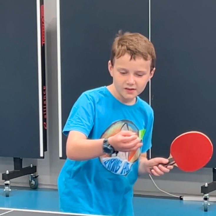 a boy in a blue t shirt is getting ready to hit a table tennis ball with a red bat