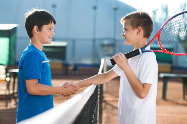 two boys are shaking hands over a tennis net