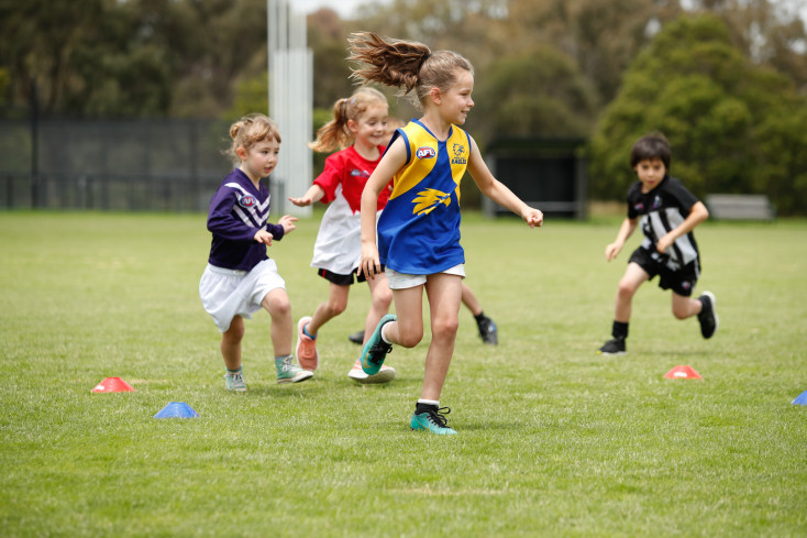 a group of girls in different coloured sports tops are running around some cones on a sports pitch