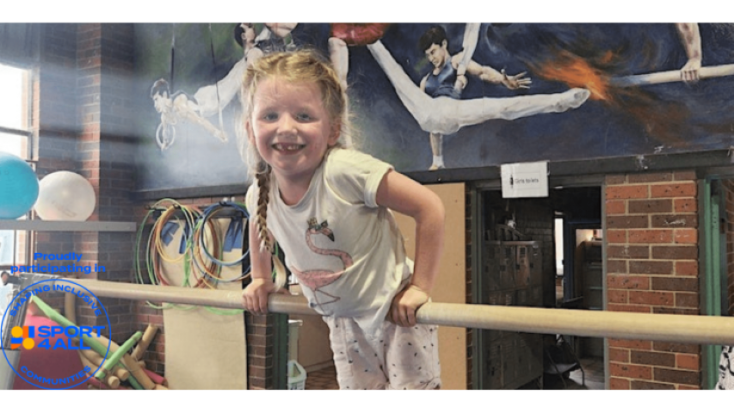 a girl is balancing on a gymnastics bar on her tummy and smiling at the camera