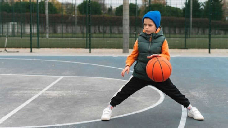 a young boy is bouncing an orange ball on an outdoor basketball court