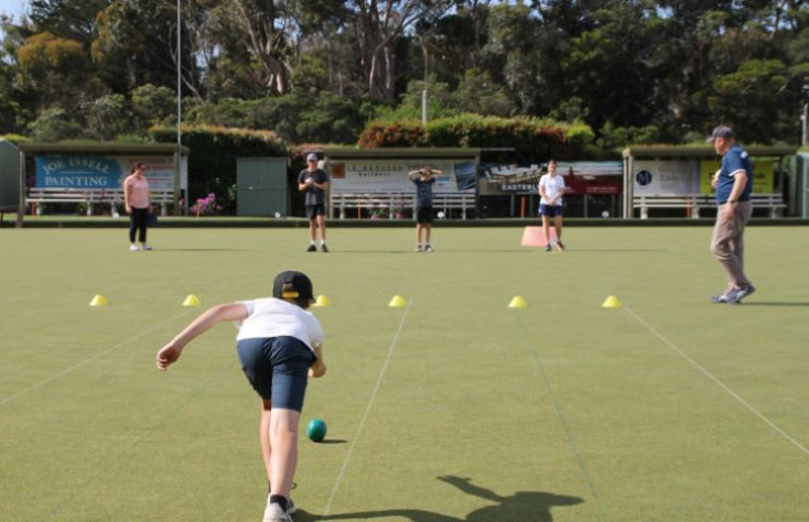 a boy is bowling down a bowling green, away from the camera