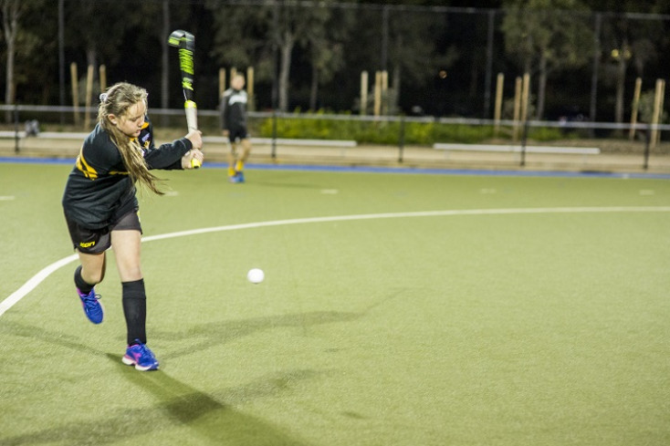 a girl wearing black sports kit is hitting a ball with a hockey stick