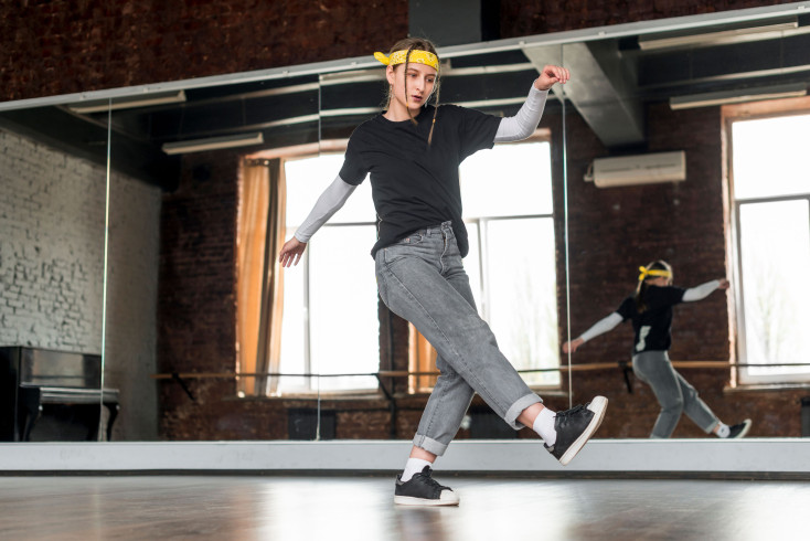 A girl wearing casual clothing is performing a hip hop move in a dance studio