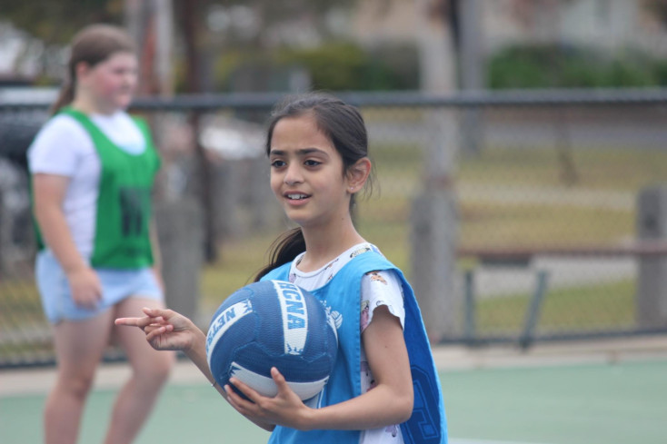 a girl wearing a blue netball bit is smiling at the camera and holding a blue and white netball