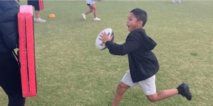 a boy holding a rugby ball is running at a tackle mat