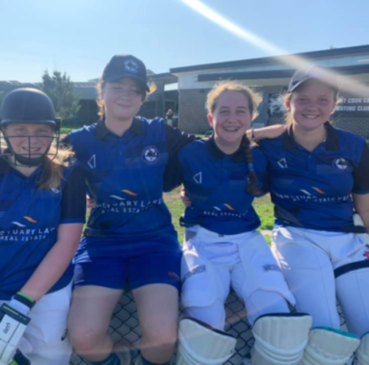 4 girls wearing blue cricket uniforms are smiling at the camera