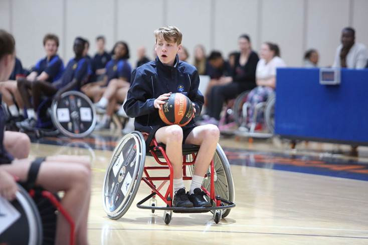 a boy wearing blue sports kit in a wheelchair is preparing to throw a basketball