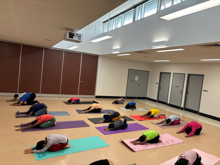 a group of children on yoga mats are kneeling back with their hands stretched out infront on the floor in a Yoga pose