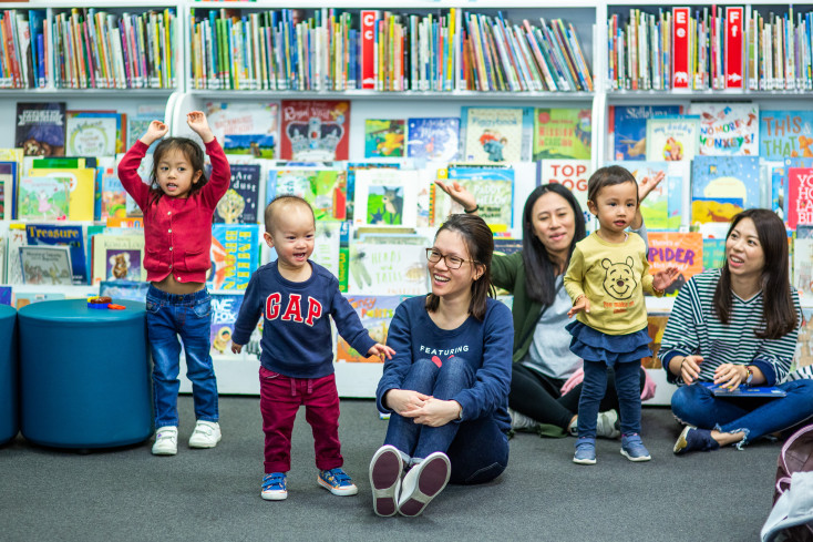 Parents and children singing and smiling in the library.