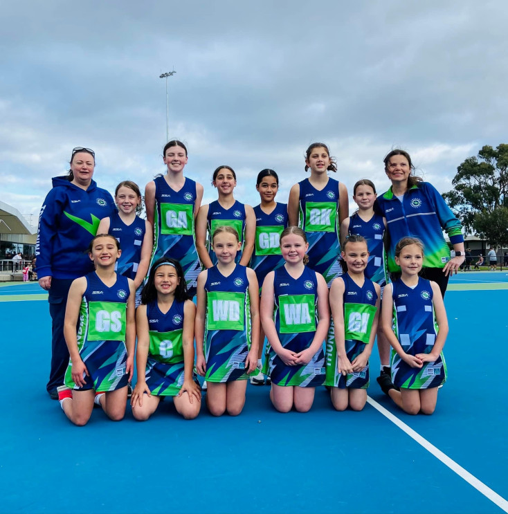 a team of netball players wearing blue and green uniforms smile at the camera