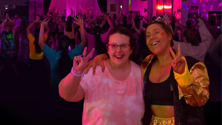 two women with their arms around each other are smiling at the camera in a darkened room