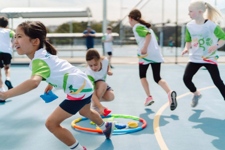 a group of kids are playing a game on a Netball court with hoops