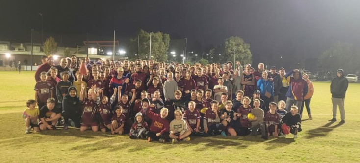 a large group of kids and adults wearing maroon sports kits are smiling at the camera.