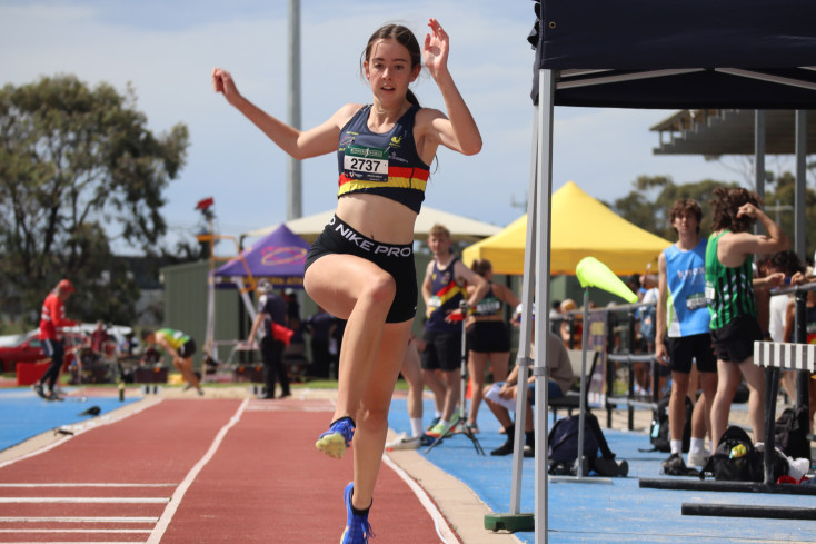 a girls wearing an athletics club top is taking off for a long jump