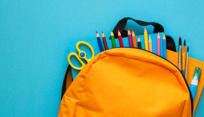 An orange school backpack with pencils and tools showing