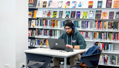 A young person using a laptop in front of the YA fiction shelves