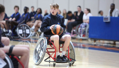 a boy wearing blue sports kit in a wheelchair is preparing to throw a basketball