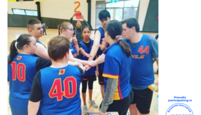 a group of people wearing blue basketball tops with red numbers on the back are standing in a circle. They have their hands in the middle.