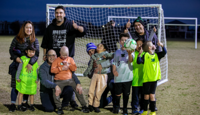 a group of adults and children are standing infront of a football goal and smiling at the camera