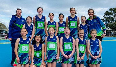 a team of netball players wearing blue and green uniforms smile at the camera