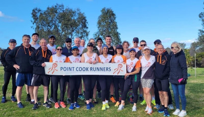 a group of people stand and smile at the camera holding a banner which says Point Cook Runners