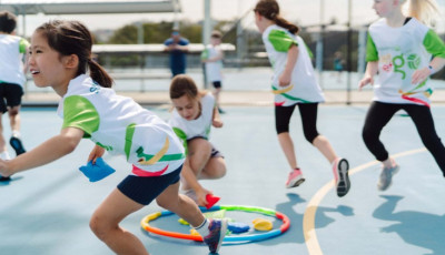 a group of kids are playing a game on a Netball court with hoops