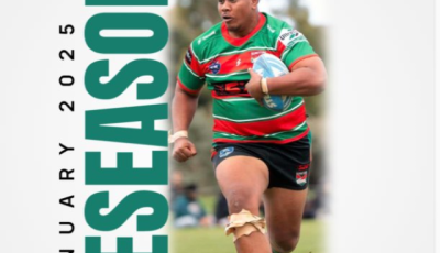 a mand wearing a red and green top is holding a rugby ball and running towards the camera