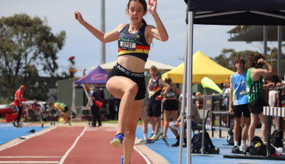 a girls wearing an athletics club top is taking off for a long jump