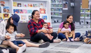 Mums and children sitting on the floor in the library and smiling.