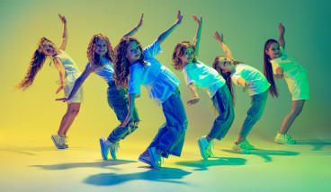 a group of kids are bending back with their arms in the air performing a dance move