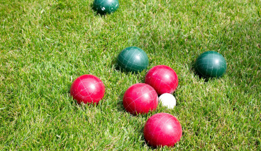 red and green lawn bowls are clustered around a white jack ball