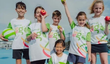a group of kids in white and green NetSetGo T shirts are cheering at the camera