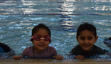 2 adults and 2 kids are in a pool smiling at the camera