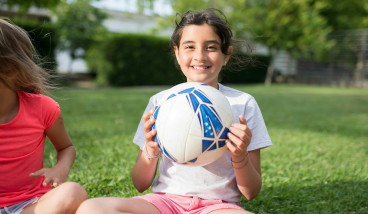 a girl in a white t shirt is holding a Football and smiling at the camera